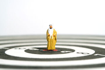 Fototapeta na wymiar Miniature people toy figure photography. A Sultan wearing yellow bihst (king cloak) standing in the center of dartboard. Isolated on white background