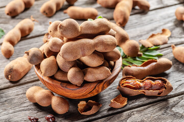Ripe tamarind fruit, leaves and some tamarind seeds on wooden table.