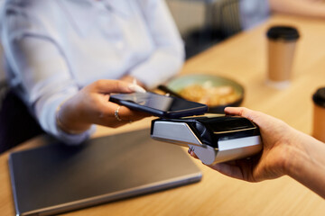 Close up of unrecognizable woman paying with smartphone in cafe and using bank payment machine, copy space