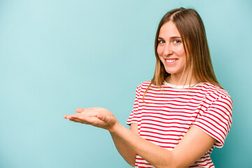 Young caucasian woman isolated on blue background holding a copy space on a palm.