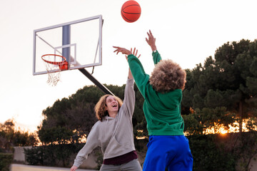 couple of friends playing basketball outdoors