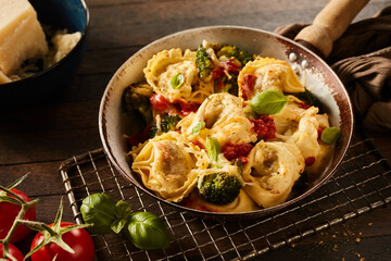 Appetizing homemade tortelloni pasta with broccoli and tomatoes on the metal grill