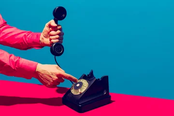 Foto op Aluminium Retro-objecten, gadgets. Vrouwelijke hand met handset van vintage telefoon geïsoleerd op blauwe en roze achtergrond. Vintage, retro mode-stijl. Pop-art fotografie. © master1305