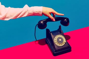 Retro objects, gadgets. Female hand holding handset of vintage phone isolated on blue and pink background. Vintage, retro fashion style. Pop art photography.