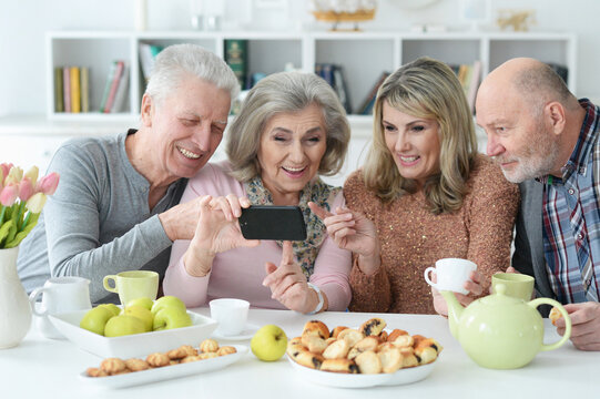 two Senior couples using smartphone during morning tea
