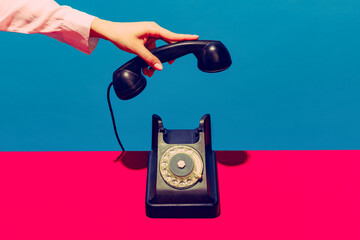 Retro objects, gadgets. Female hand holding handset of vintage phone isolated on blue and pink background. Vintage, retro fashion style. Pop art photography. - obrazy, fototapety, plakaty