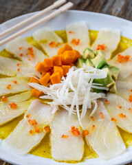 Close-up shot of Tiradito de Pescado (Peruvian Sashimi), with wooden chopsticks in white plate
