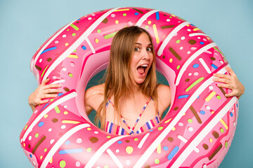 Young caucasian woman holding air mattress isolated on blue background
