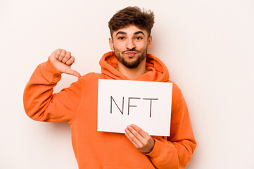 Young hispanic man holding a NFT placard isolated on white background feels proud and self...