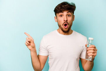 Young hispanic man holding a bottle of water isolated on white background pointing to the side