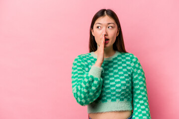 Young Chinese woman isolated on pink background is saying a secret hot braking news and looking...