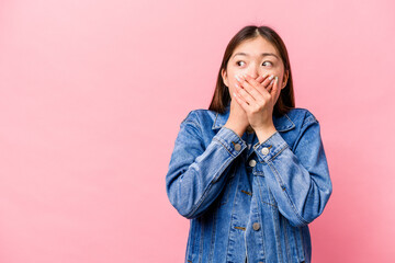 Young Chinese woman isolated on pink background thoughtful looking to a copy space covering mouth with hand.