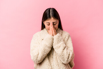 Young Chinese woman isolated on pink background praying, showing devotion, religious person looking for divine inspiration.
