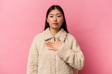 Young Chinese woman isolated on pink background taking an oath, putting hand on chest.