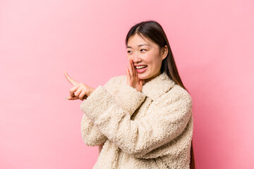 Young Chinese woman isolated on pink background saying a gossip, pointing to side reporting something.