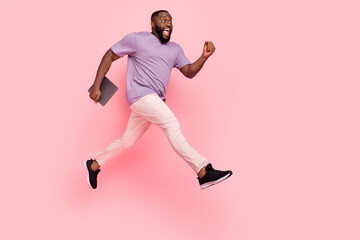 Photo of excited impreesed guy wear purple t-shirt jumping high holding modern device isolated pink...
