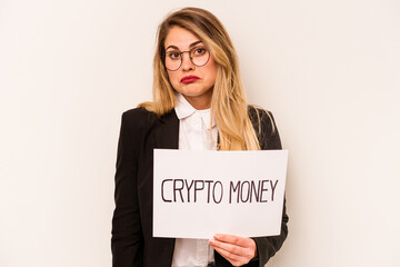 Young business caucasian woman holding a crypto money placard isolated on white background shrugs shoulders and open eyes confused.