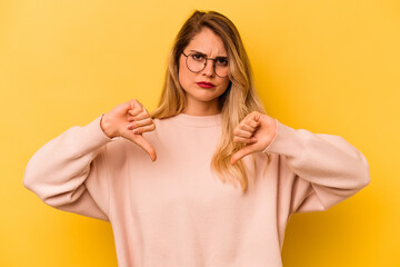 Young caucasian woman isolated on yellow background showing a dislike gesture, thumbs down....
