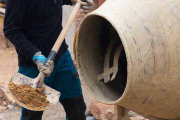 Close up of unrecognizable man throwing gravel into a concrete mixer machine