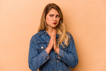 Young caucasian woman isolated on beige background praying, showing devotion, religious person looking for divine inspiration.