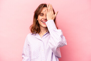 Young caucasian woman isolated on pink background having fun covering half of face with palm.