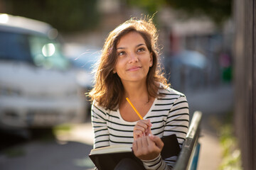 Close up beautiful young woman smiling and holding book and pen while looking away