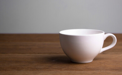 Front view of  white ceramic coffee cup on a brown rustic wooden table.