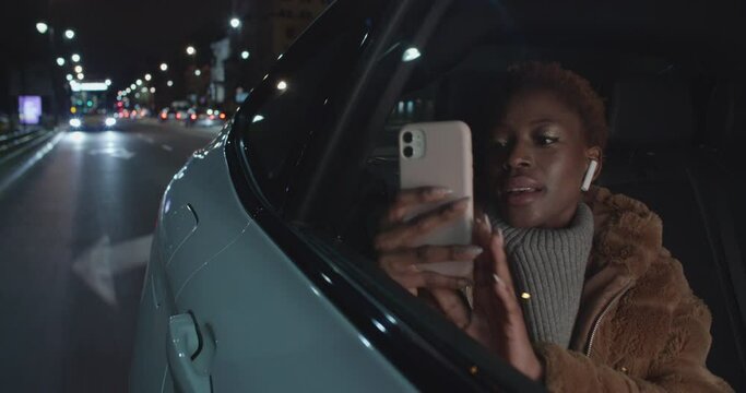 Young Beautiful Black woman with earphones riding in taxi uber in night time
