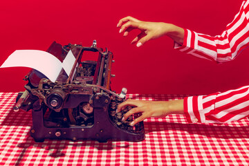 Pop art photography. Female hand using retro typewriter isolated on bright red background. Vintage,...