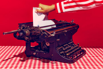 Pop art photography. Female hand using retro typewriter isolated on bright red background. Vintage, retro style.