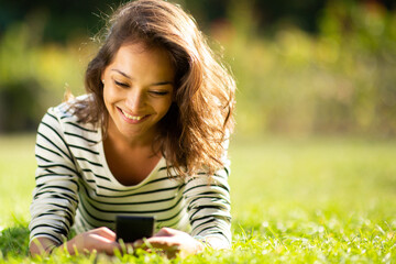 smiling young woman relaxing in park looking at mobile phone