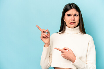 Young caucasian woman isolated on blue background shocked pointing with index fingers to a copy space.