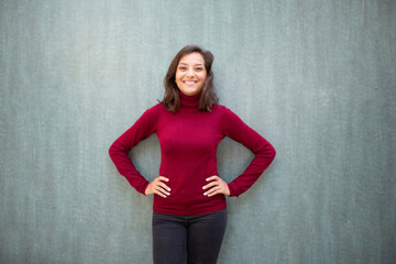 smiling young woman posing with hands on hip against green wall