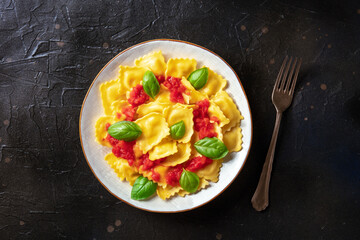 Ravioli with tomato sauce and fresh basil on a plate. Healthy Italian meal, overhead shot on a black slate background