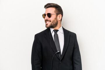 Young caucasian bodyguard man isolated on white background looks aside smiling, cheerful and...