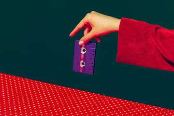 Female hand holding tape recorder cassette isolated on green and red background. Vintage, retro fashion style. Pop art photography