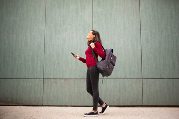 Full length young woman walking with bag and cellphone by wall