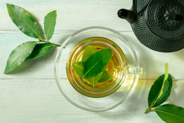 Bay leaf tea. Fresh laurel leaves infusion with a cup and a teapot, on a rustic wooden background,...