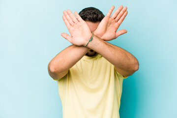 Young caucasian man isolated on blue background keeping two arms crossed, denial concept.