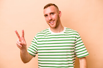 Naklejka premium Young caucasian man isolated on beige background showing victory sign and smiling broadly.