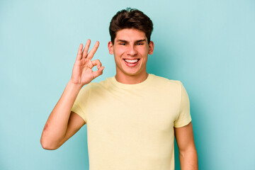 Young caucasian man isolated on blue background cheerful and confident showing ok gesture.