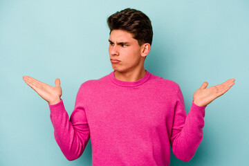 Young caucasian man isolated on blue background confused and doubtful shrugging shoulders to hold a...