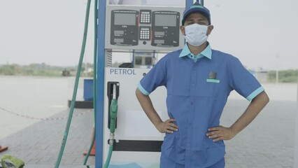 Worker with unifrom and medical face mask confidently standing by looking camera at gas filling or petrol station - concept of busines reopen, back to work and safety measures due to coronavirus
