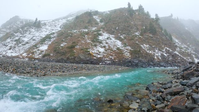 4K shot of Chenab River flowing during the snowfall in the mountains at Sissu in Himachal Pradesh, India. View of blue coloured river during the snowfall after crossing the Atal Tunnel.	