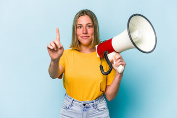 Young caucasian woman holding a megaphone isolated on blue background showing number one with finger.