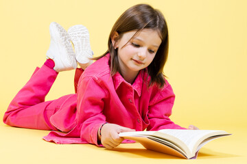 Little girl laying on yellow background and reading a book.