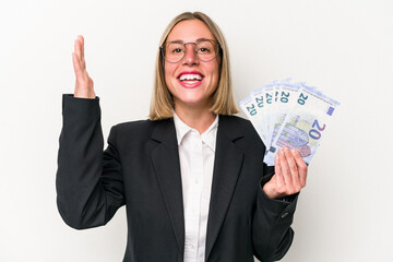 Young business caucasian woman holding banknotes isolated on white background receiving a pleasant surprise, excited and raising hands.