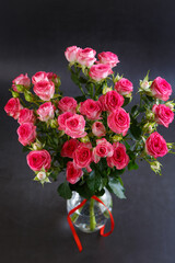 Obraz premium Beautiful bouquet of pink (red) roses bushes with water drops on a black background. Selective focus, close-up.