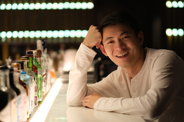 portrait of one smiling Asian young man sitting at bar counter, looking at camera at night