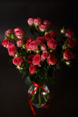Beautiful bouquet of pink (red) roses bushes with water drops on a black background. Selective focus, close-up.